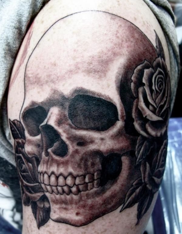 Tattoo of skull and black roses occupy the entire arm of this man, thanks to coloring the cavities of the eyes in black it has managed to reach a good depth of the eyes and the petals of the roses are also very well achieved