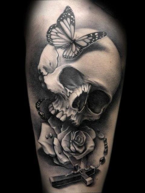 Tatuaje de calavera sobre la que se ha posado una mariposa, a decir verdad, de este tatuaje lo que más nos llama la atención no es la cruz, ni el craneo, ni la rosa, sino la mariposa porque se ha conseguido una postura basatnte realista de la mariposa y un dibujo muy bonito