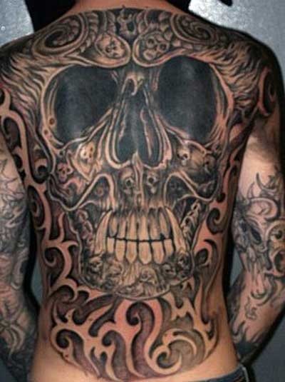 Tatuaje enorme de una calavera que ocupa toda la espalda y que se completa con grandes llamas de fuego en las pestañas y unos motivos tribales que rodean a todo el tatuaje, un tatuaje sin duda, cuanto menos singular