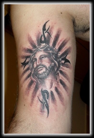 Tatuaje en el bíceps de la cara de Jesucristo adornado con unos tribales que poco pegan con este tatuaje, pero que seguro a su dueño le encanta, nosotros no podemos decir lo mismo, a pesar de que nos gusten mucho los tatuajes cristianos