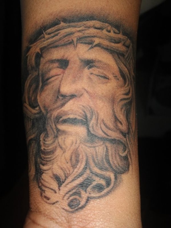 Tattoo del rostro de Jesucristo con los ojos cerrdos y gestos de sufrimiento, realizado sobre el antebrazo y que nos recuerda el gran dolor por el que pasó el Hijo de Dios para salvar al mundo