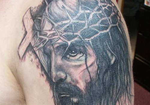 Tatuaje del rostro de Jesucristo, que versa su originalidad en dibujar sólo la mitad de la cara del Señor y en un lado una cruz de madera