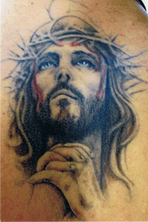 Tatuaje de Jesucristo con una peculiar nariz y una corona de espinas diferente a la que acostumbramos a ver, ya que las espinas son muy largas y parecen no estar clavándole demasiado, aunque hay otras como muestra la sangre que se ha tatuado, que sí recuerdan lo que el Señor sufrió por purgar los pecados