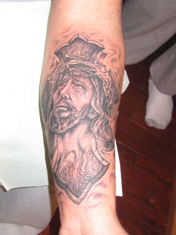 Tatuaje de una cruz de la que sobresale Cristo llorando y mirando al cielo hacia Dios, un buen trabajo del que se podía haber mejorado algo más la corona de espina que se le ha tatuado a Jesucristo