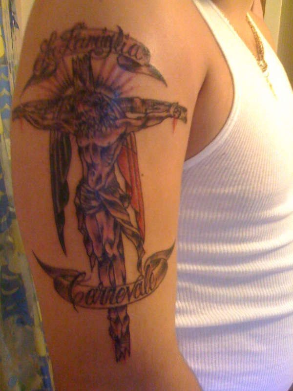 Tattoo of the crucified Christ and to whom a sheet has been placed on the cross that gives an air of wings, to this tattoo the words The Carnevale family or something similar have been added, since we cannot identify the words correctly be tattooed with great skill