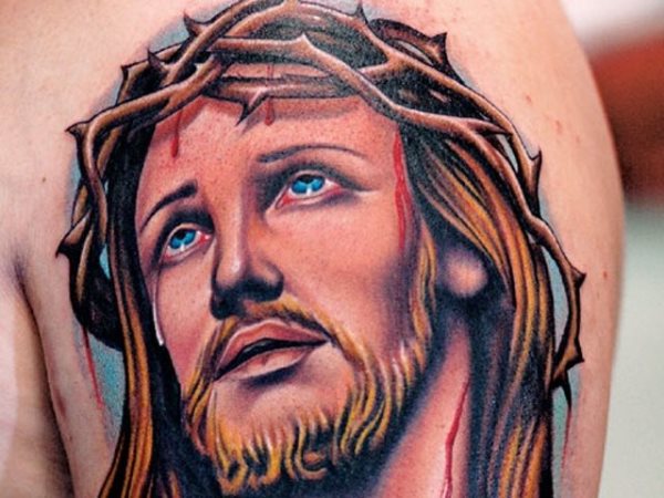 Color tattoo of a Christ with blond hair and blue eyes, from which the drop of blood drops from the crown of thorn and to which tears have been tattooed on one of his eyes, a different Christ than we are accustomed to seeing along the history