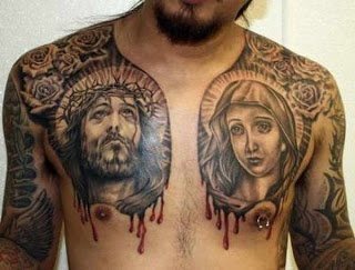 Tatuaje en el pecho de Jesucristo a un lado y en el otro lado la Virgen María, ambos tatuajes se les ha tatuado sangre chorreando bajo el pecho y también podemos apreciar grandes tatuajes en los brazos