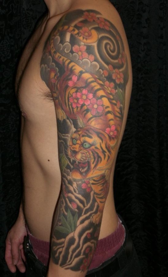 Manga style tattoo, that is, covering the entire arm with the image of a tiger adorned with colorful pink flowers and a background of black clouds