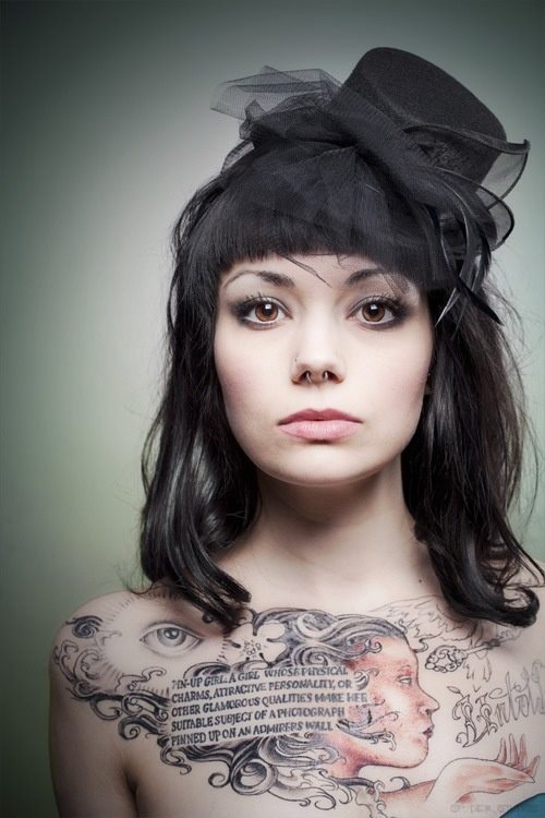 Complex of tattoos on the chest of this girl, in which we can appreciate a text that does not identify the letters very well, a woman's head with a long wavy hair that looks great on the tattoo, an eye and other elements