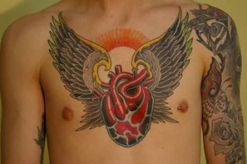 Tatuaje de un corazón al que se le han hecho algunas de sus venas y arterias, dotándole de un carácter muy realista y para el que se ha envuelto con unas grandes alas negras, de plumas pequeñas y finas, acabadas en tonos verdes y amarillos