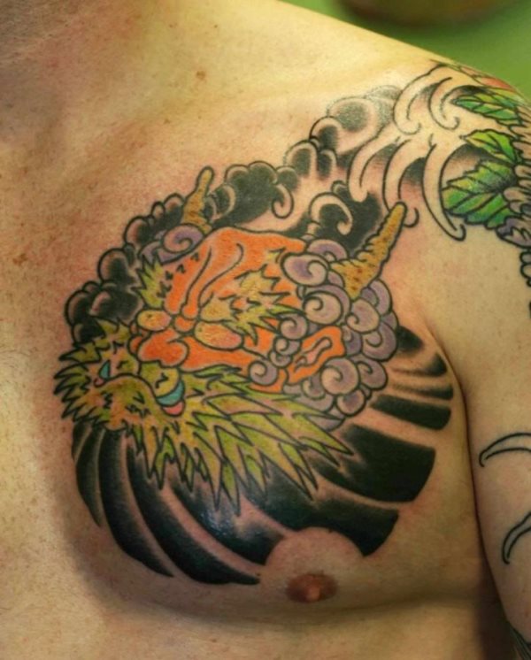 Very colorful tattoo on the chest of a head with colored horns, green beard, narajna and light blue teeth, which has purple hair and from which smoke stands out that makes the background times to reach the shoulders, where another is appreciated tattoo